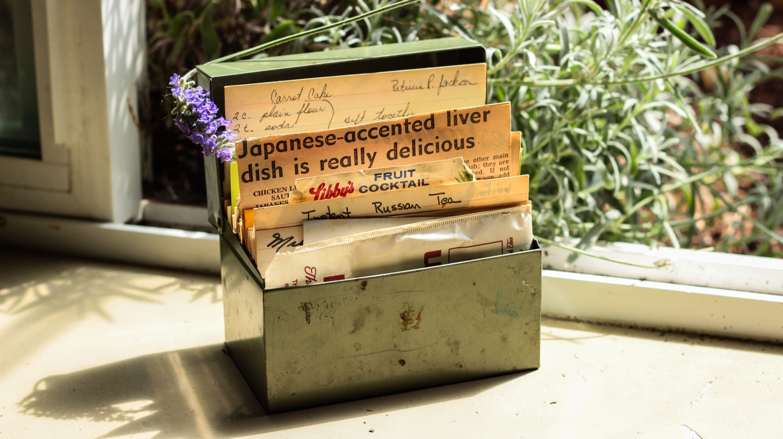 A metal box full of recipes cut from newspapers and backs of cans. One headline reads, "Japanese-Accented Liver Dish Is Really Delicious"