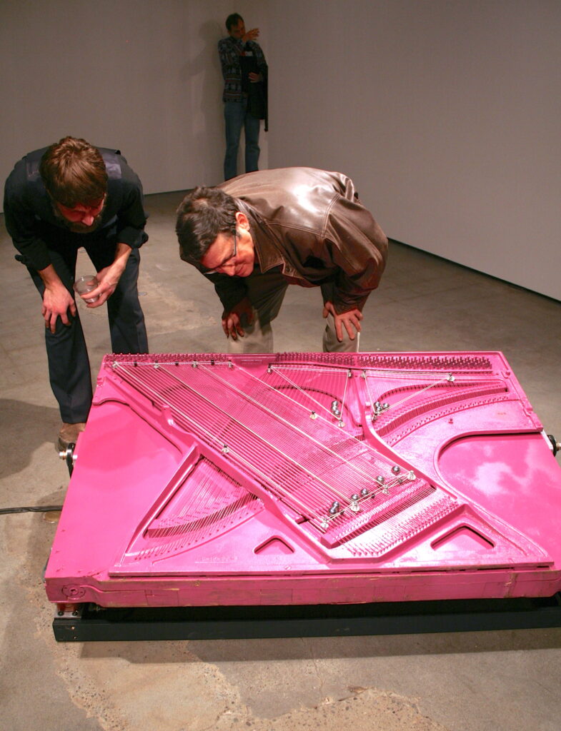 two men crouch over a hot pink platform covered in grooves for steel balls to run through and create music